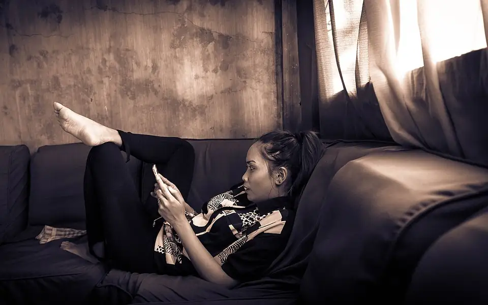 Woman checking her phone on a couch, representing mindful mobile gaming time